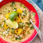 A overview of white chili topped with cheese, lime, and tortilla strips.