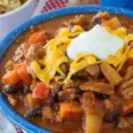 A close up of a bowl of chili topped with shredded cheese and sour cream.