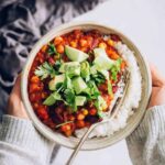 Chili in a bowl with rice topped with cilantro and avocado.