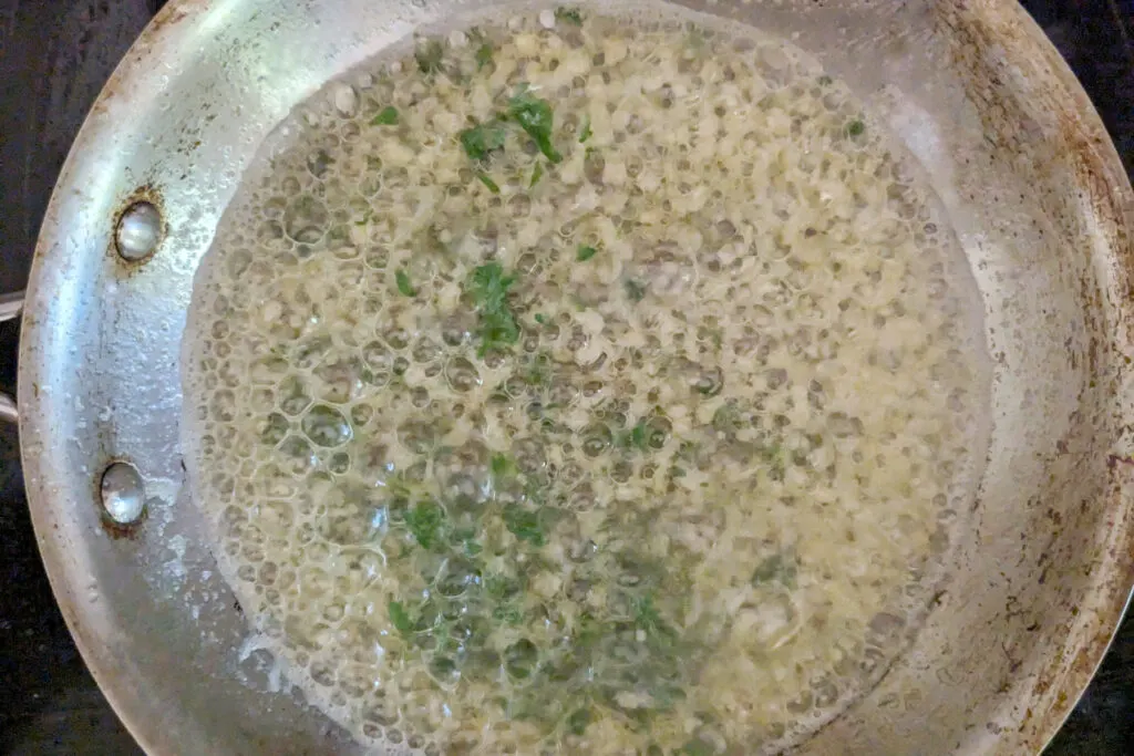 Butter, garlic, and parsley sautéing in a pan.