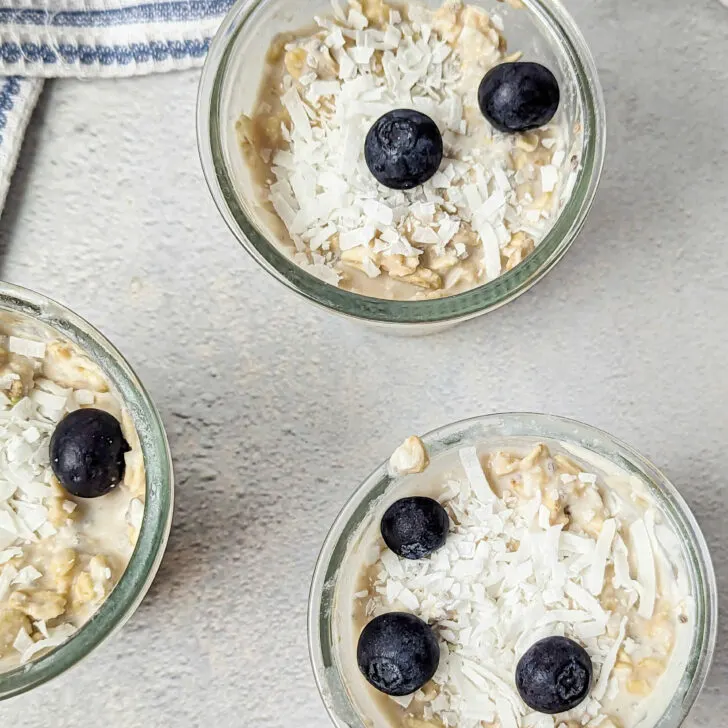 Three containers of overnight oats with coconut milk topped with fresh blueberries.