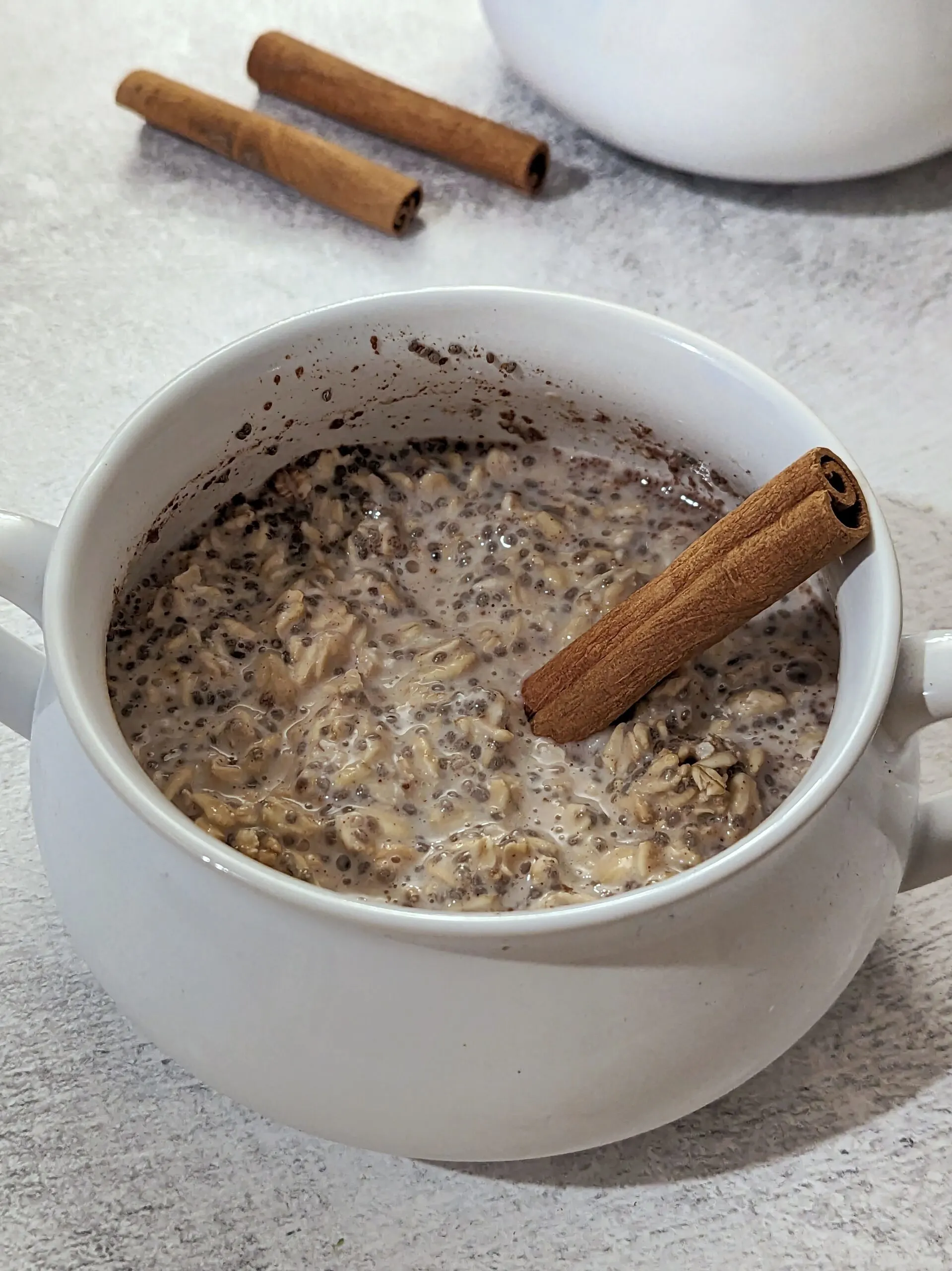 A bowl of cinnamon overnight oats with cinnamon sticks stuck into it.