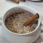 A bowl of cinnamon overnight oats garnished with a cinnamon stick.