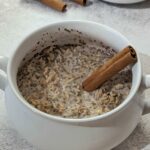 A bowl of cinnamon overnight oats garnished with a cinnamon stick.
