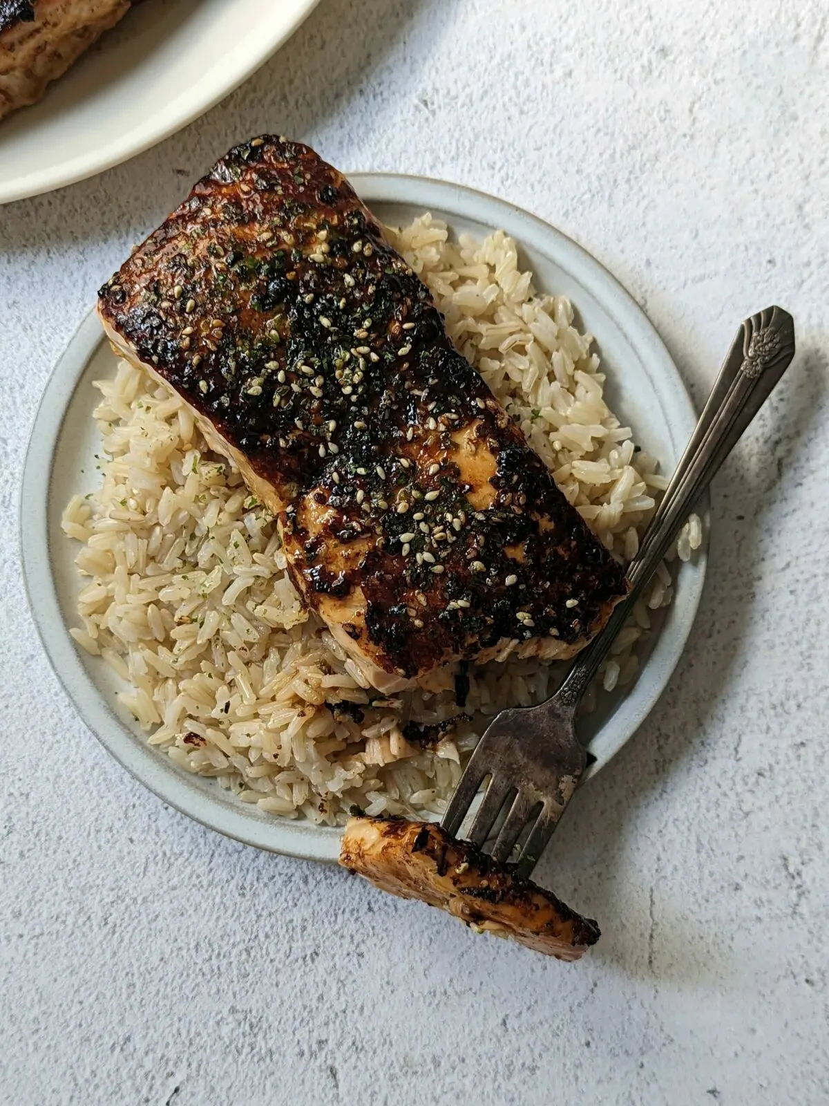 A fillet of furikake salmon cut open with a fork and served on a bed of rice.