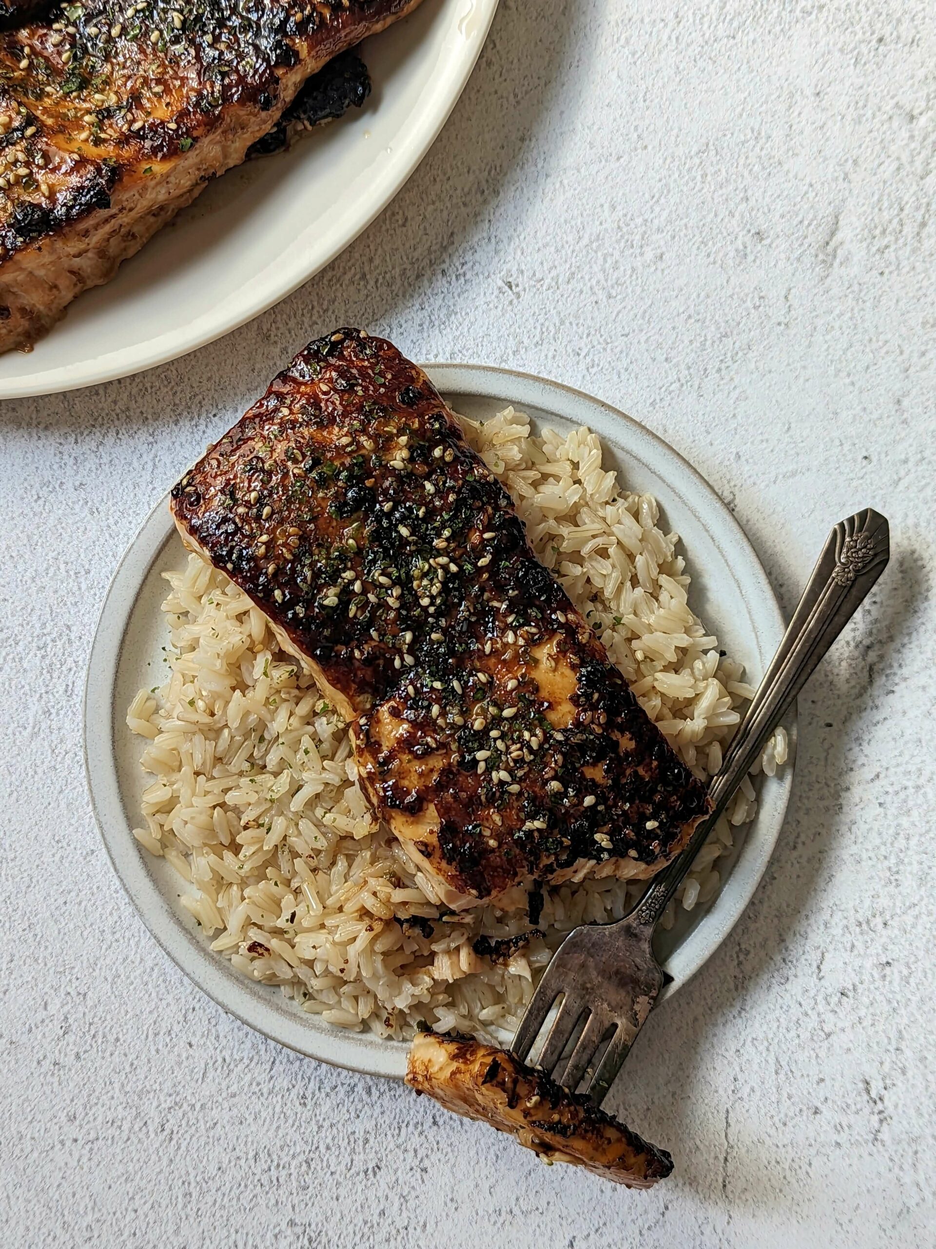 A fillet of furikake salmon cut open with a fork and served on a bed of rice.