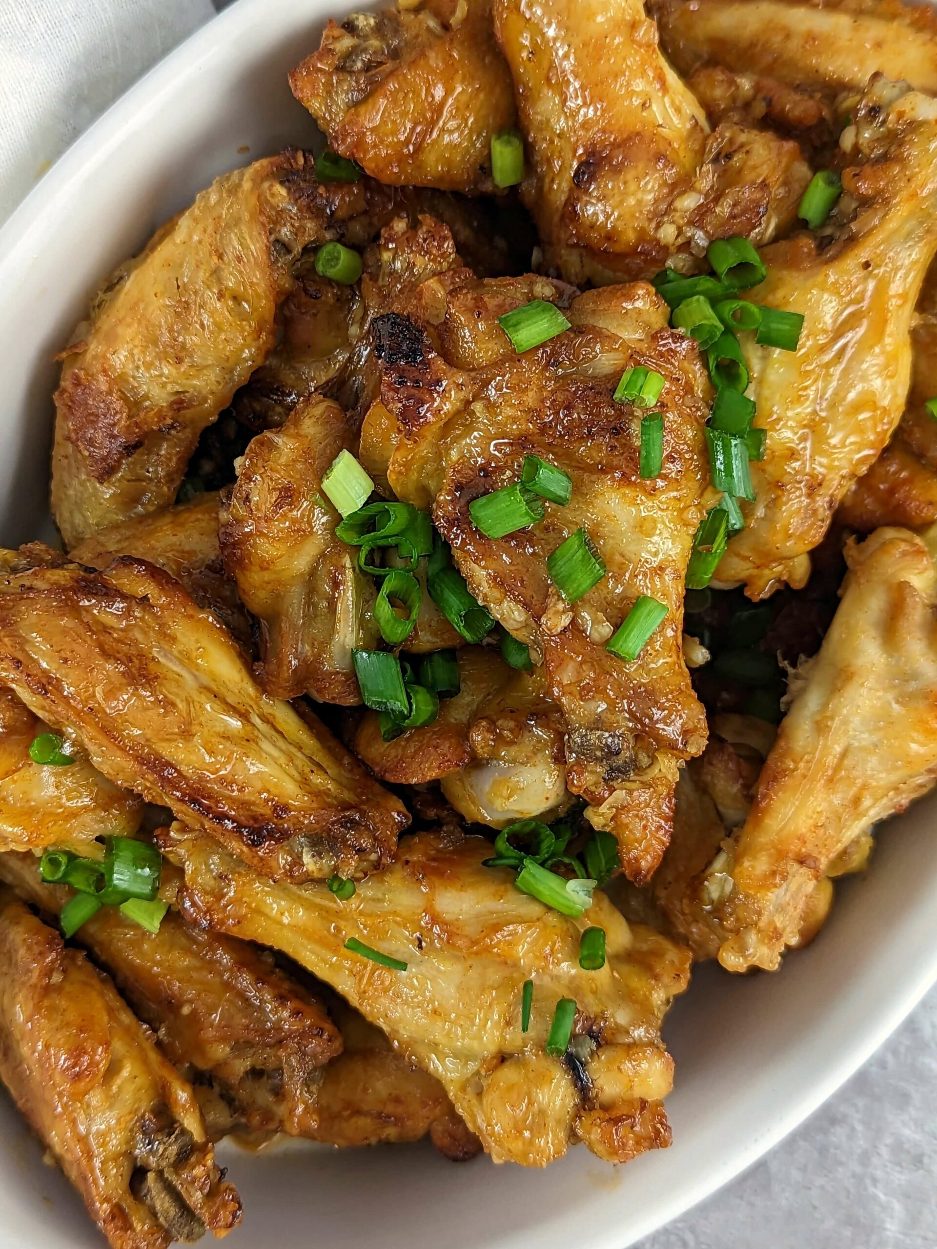 Honey garlic chicken wings in a serving dish and garnished with scallions. 