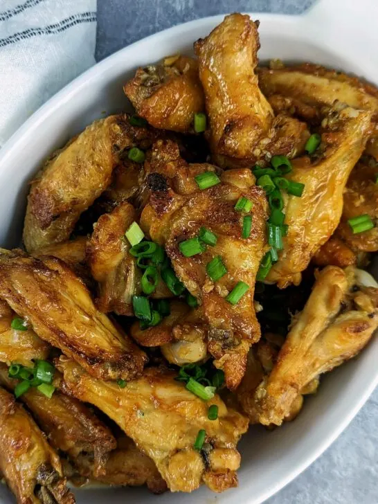 Honey garlic chicken wings in a serving dish and garnished with scallions.
