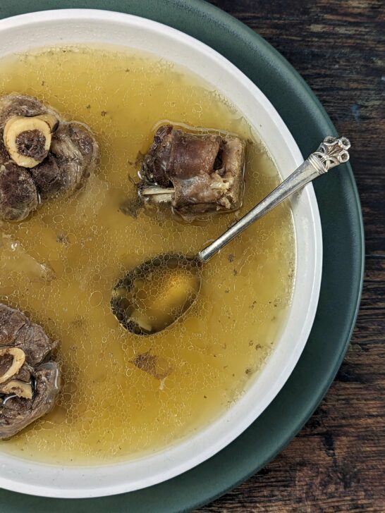 A wide bowl of mutton soup with a spoon in it.