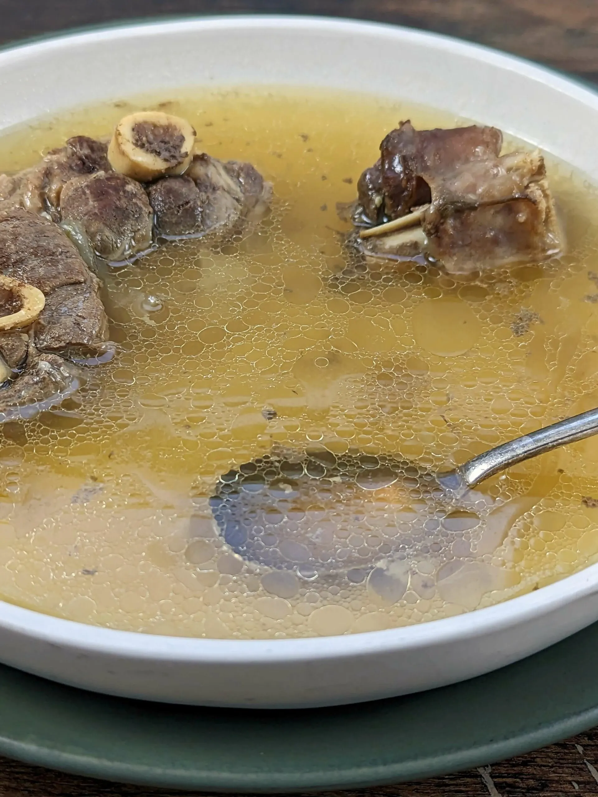 A close up of a bowl of Mutton Soup with a spoon in it.