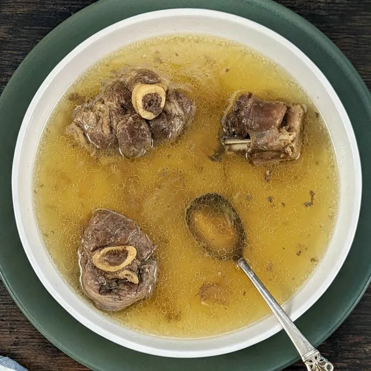 A wide bowl of mutton soup with a spoon in it.