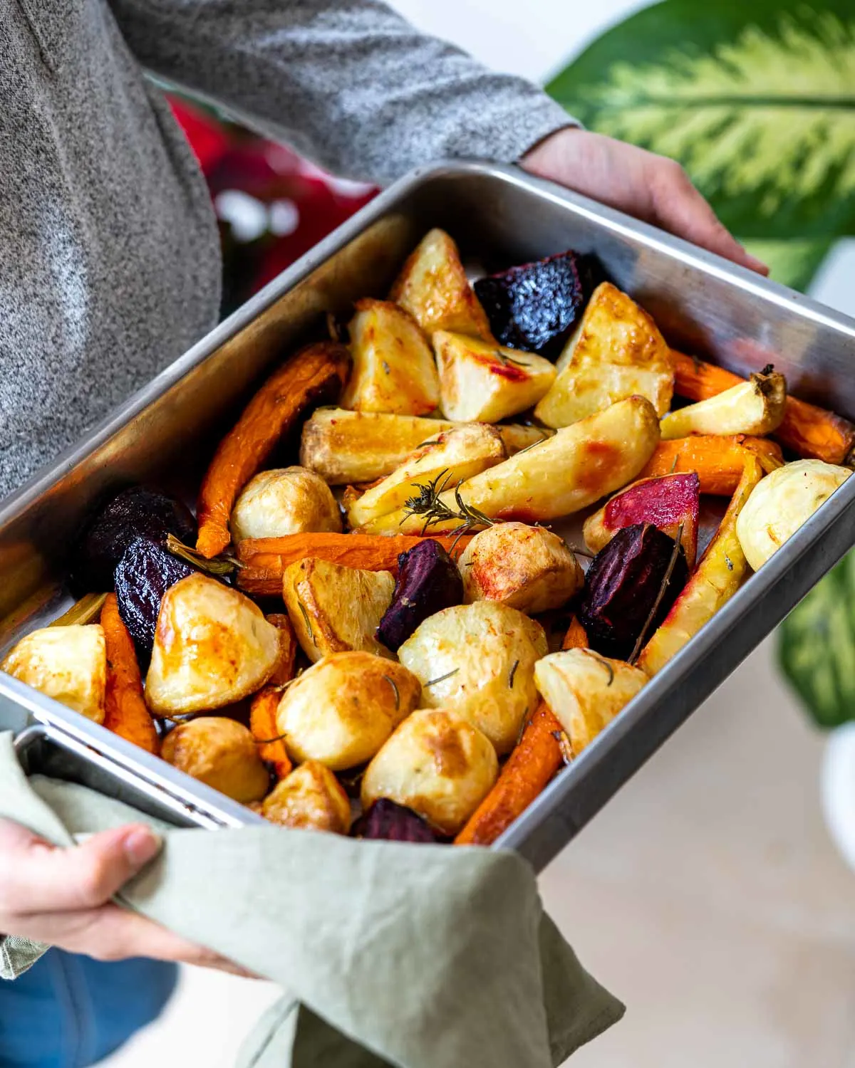 Hands holding a roasting pan of vegetables.