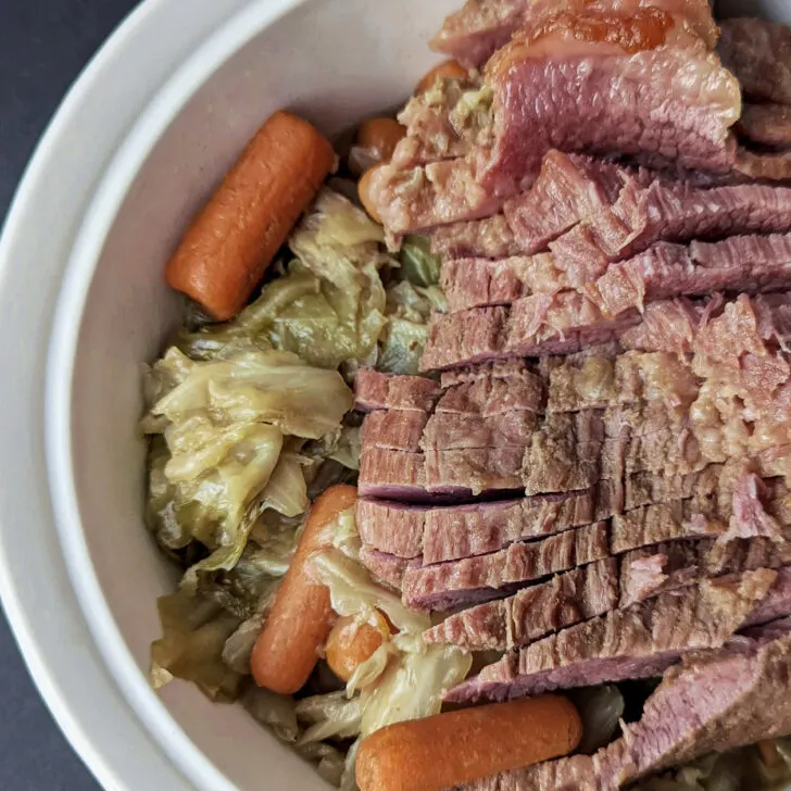 Onions, potatoes, and carrots are in a baking dish and topped with slices of tender corned beef.