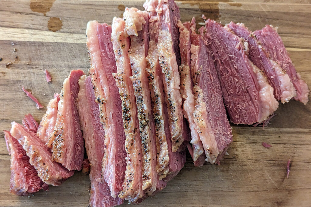 Corned beef brisket thinly sliced on a cutting board.