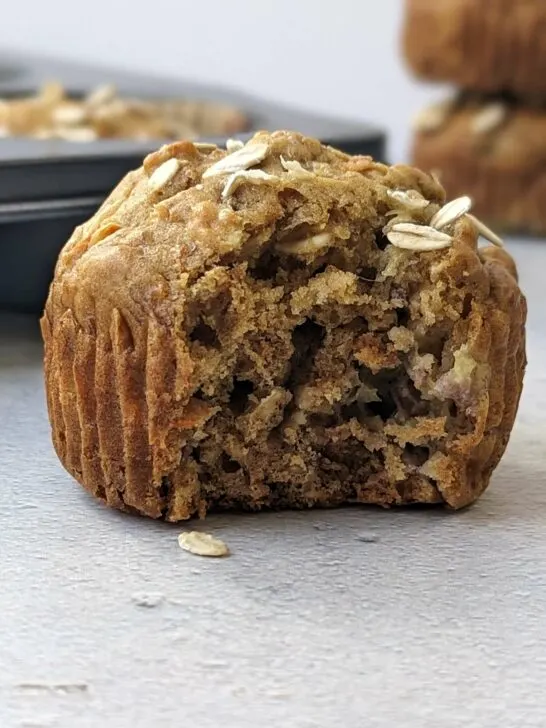 A close up of a banana carrot muffin with a bite in it and muffins in the background.