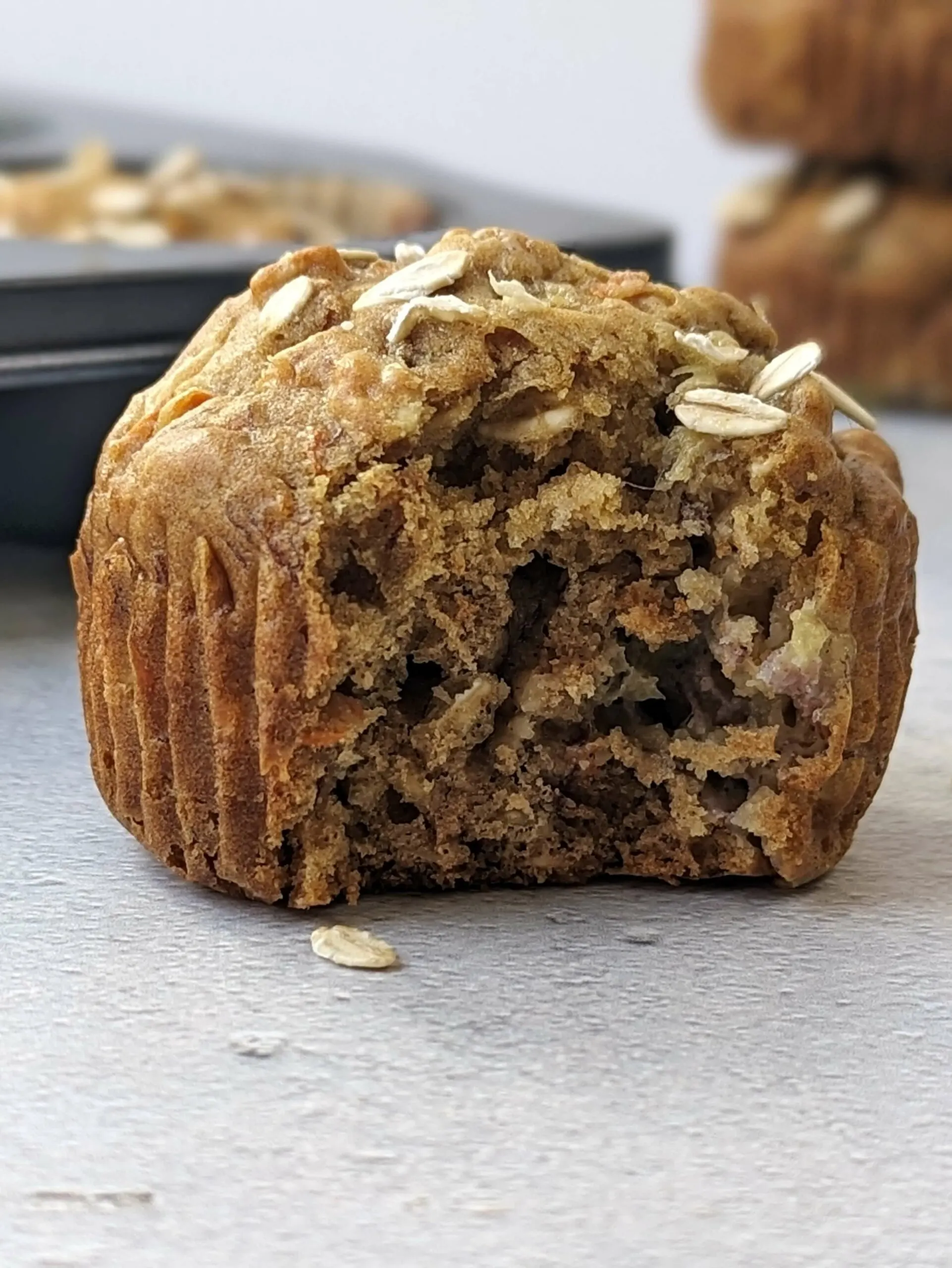 A close up of a banana carrot muffin with a bite in it and muffins in the background.