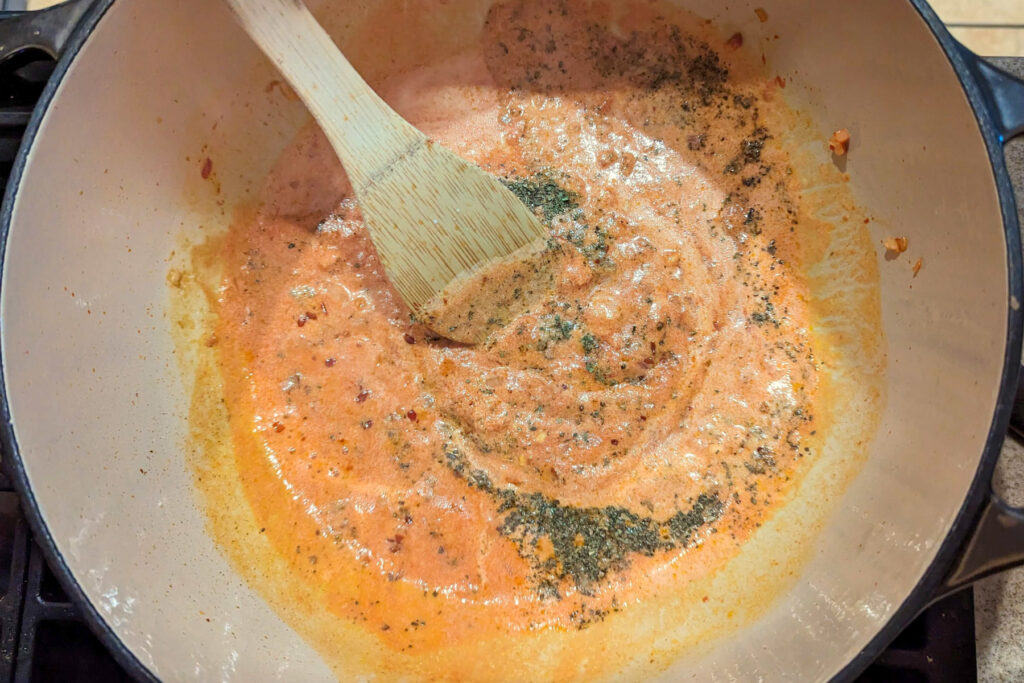 A spoon stirring heavy cream and spices into the sauce.