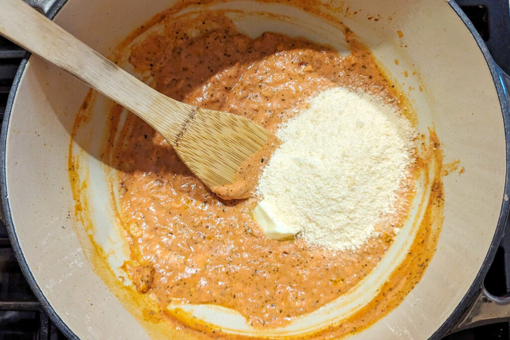 A spoon stirring butter and parmesan into the sauce.