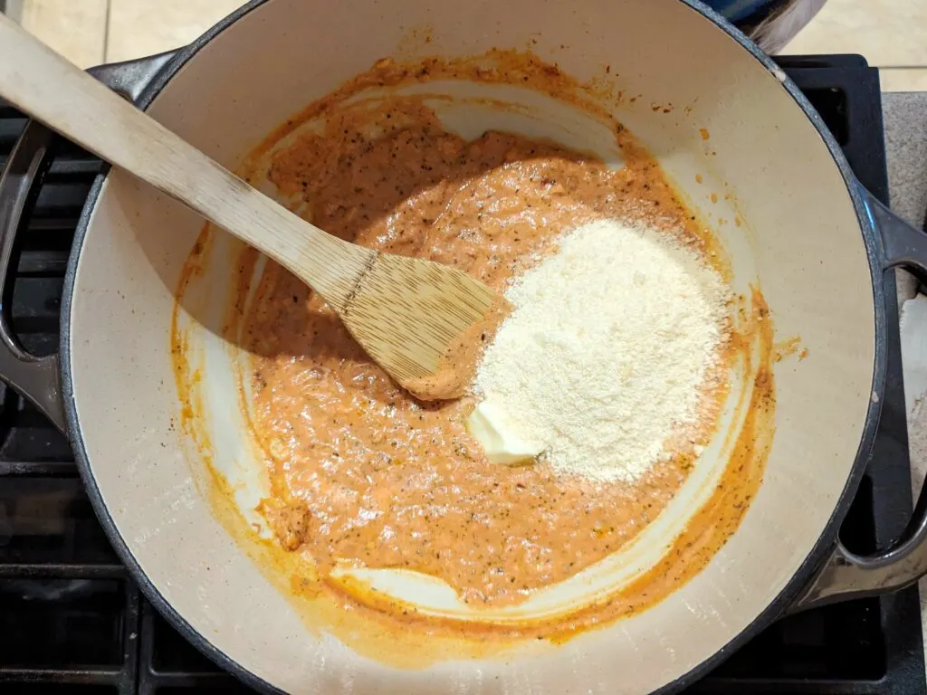 A spoon stirring butter and parmesan into the sauce.