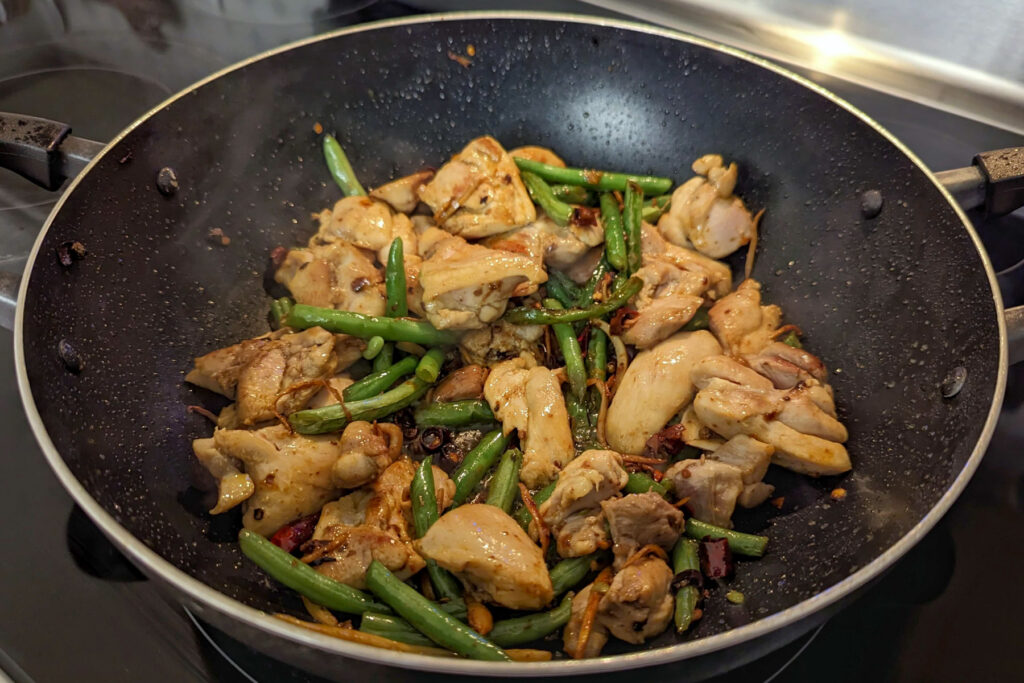 Chicken cooking in a wok with vegetables.