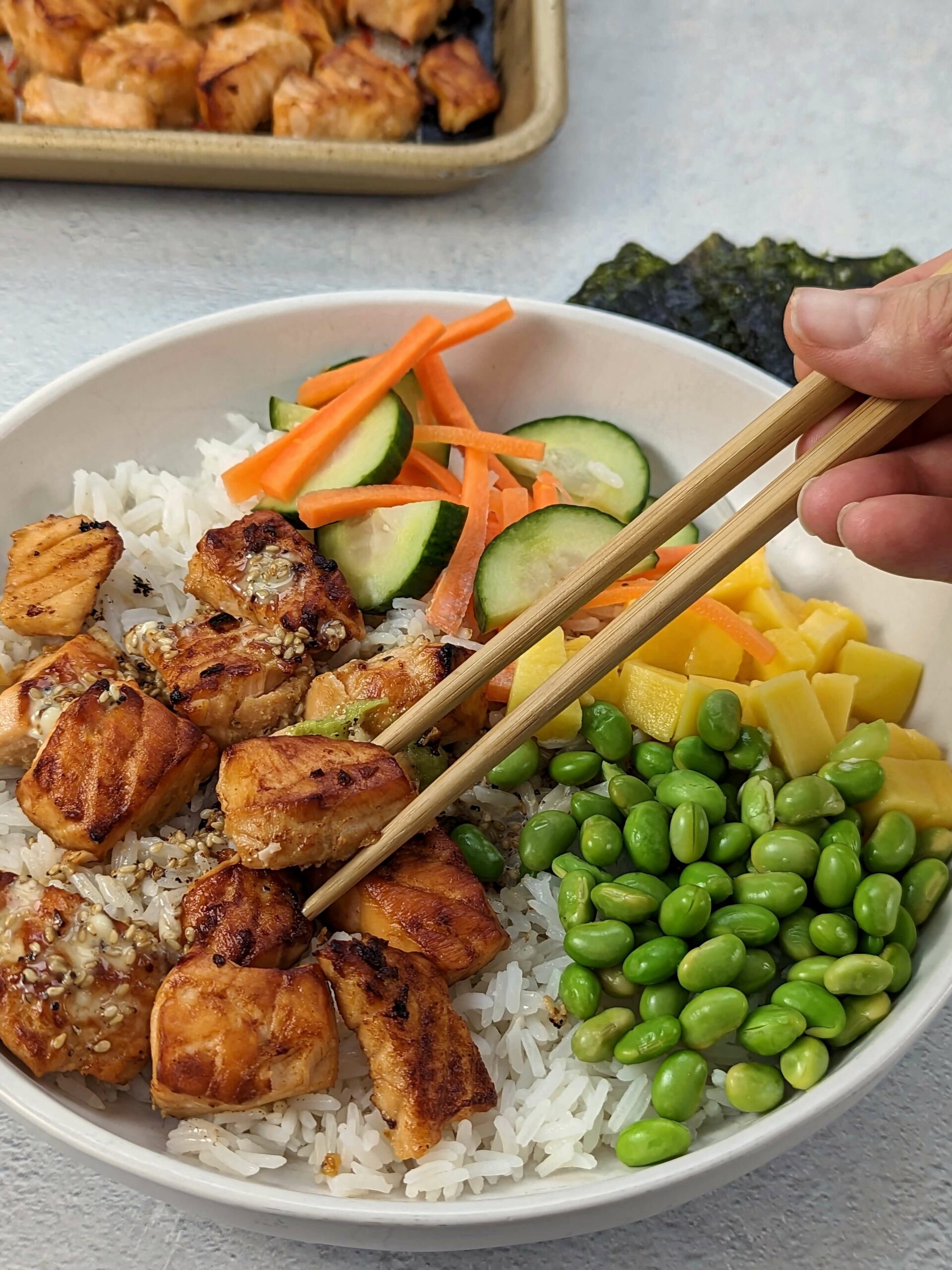 A sesame salmon bowl with seaweed and a rimmed baking sheet in the background.