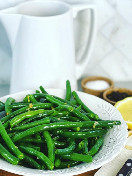 A close up of green beans with serving dishes in the background.