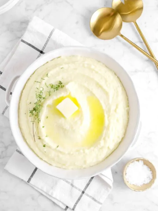 A serving bowl of mashed potatoes topped with melted butter and herbs.