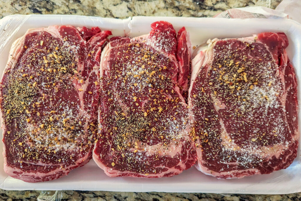 Seasoned ribeye steaks on a tray.