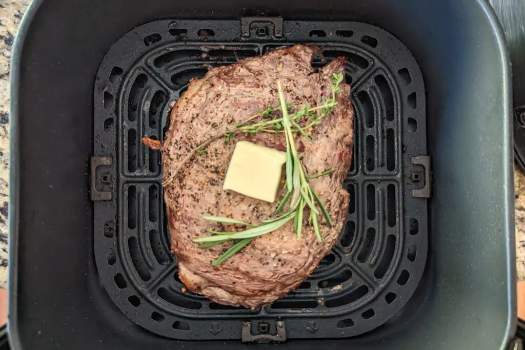 A ribeye steak with herbs and butter in an air fryer.