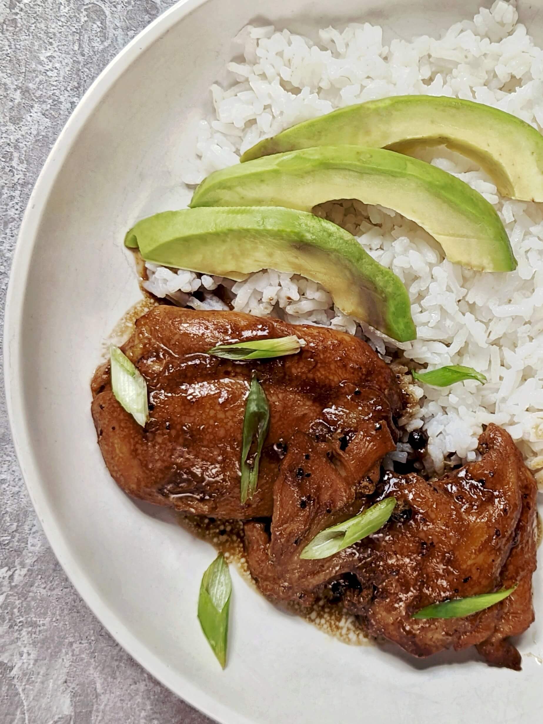 Adobong Manok on a plate with white rice and avocado slices.