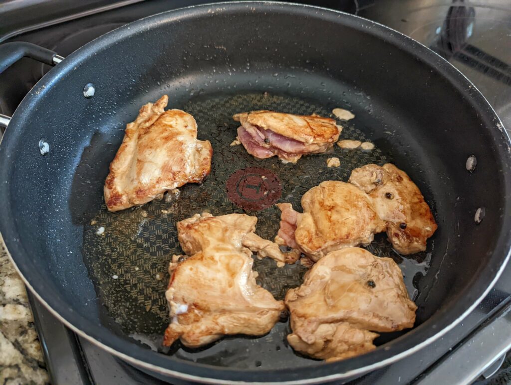 Chicken thighs browning in a pan with oil.
