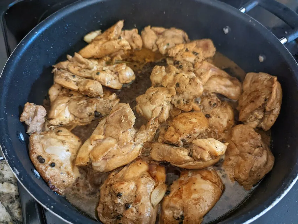 Chicken thighs in a pan with the sauce ingredients added.