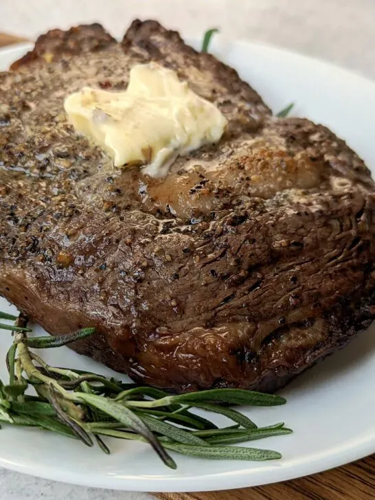 A ribeye steak topped with butter and garnished with fresh rosemary.