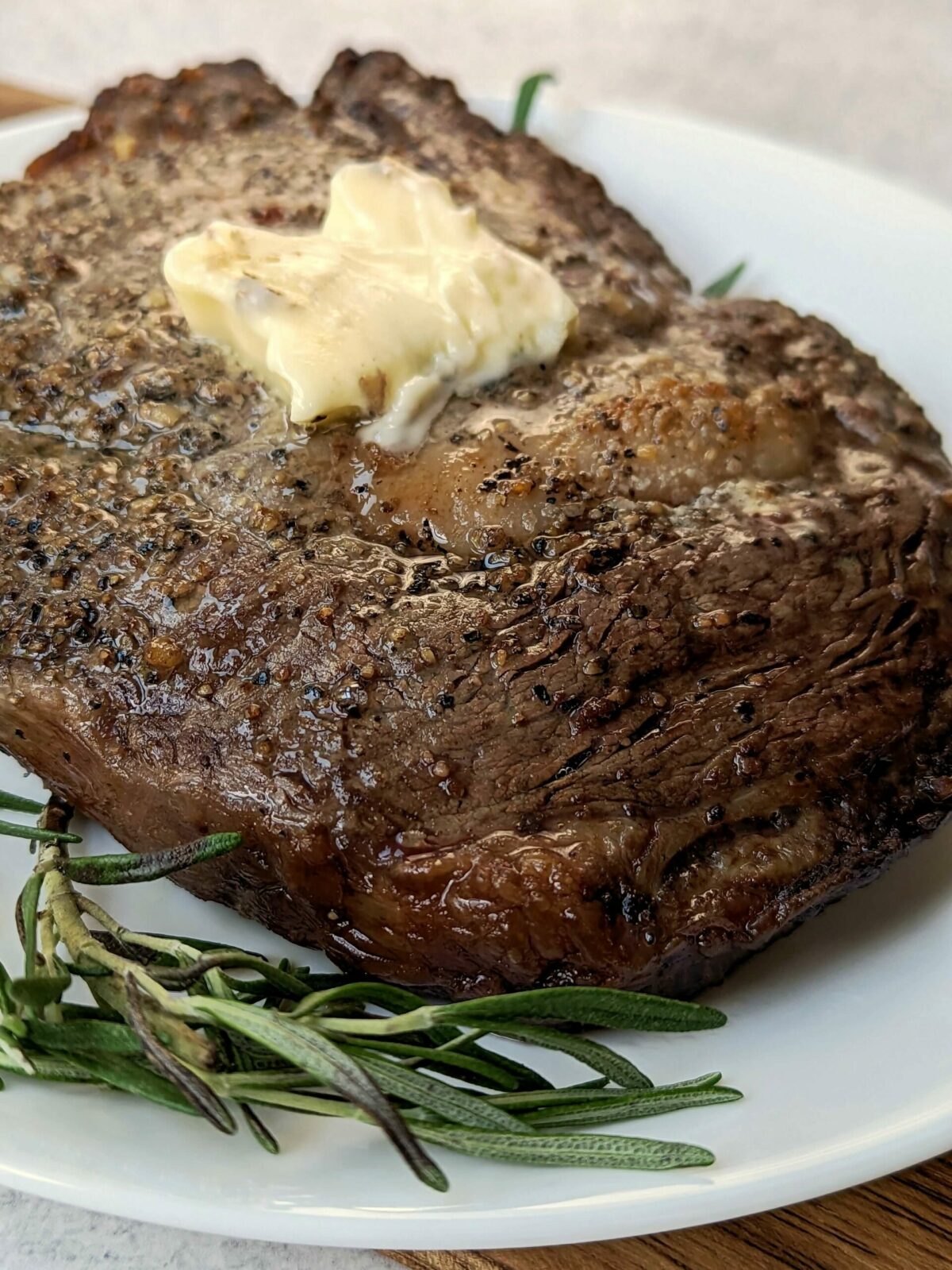 A ribeye steak topped with butter and garnished with fresh rosemary.