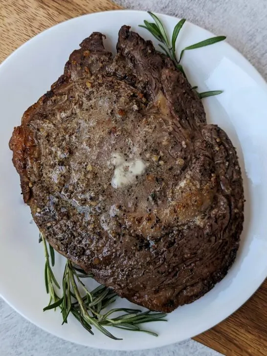 A air fryer ribeye steak topped with melted butter and garnished with fresh rosemary.