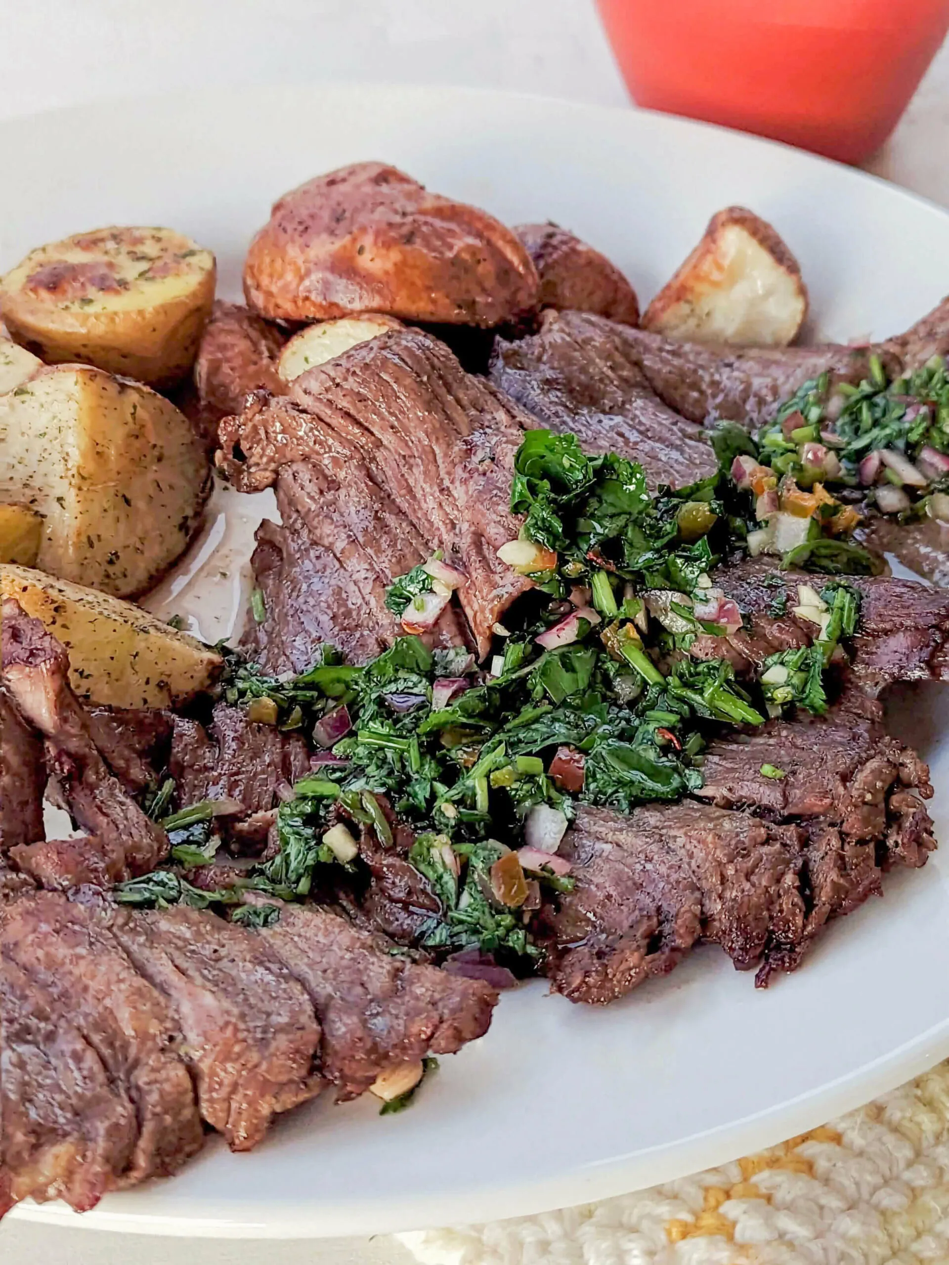 Air fryer skirt steak topped with chimichurri with potatoes in the background.