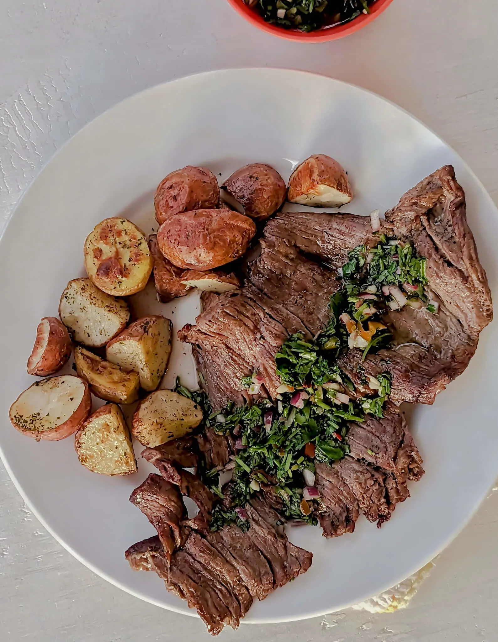 Air fryer skirt steak topped with chimichurri with potatoes in the background.