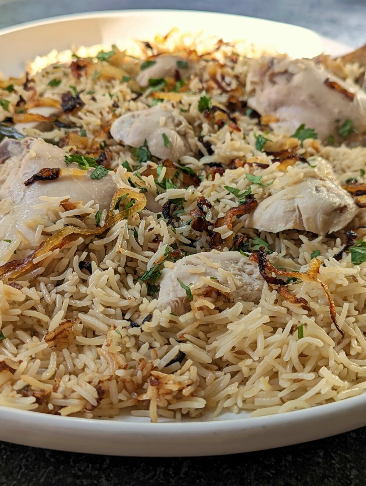 A close up of a large platter of Chicken Yakhni Pulao topped with chopped cilantro.