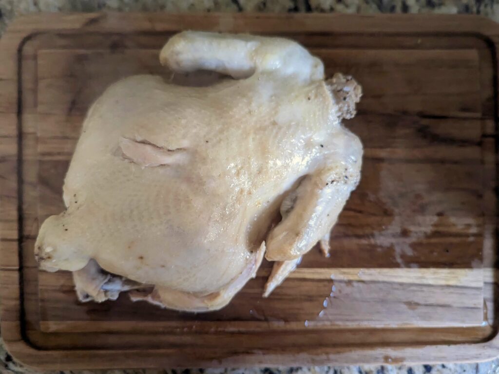 A whole chicken on a cutting board to be broken down.