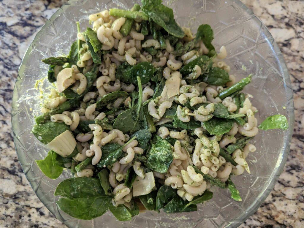 Pesto added to the vegetables in a mixing bowl.