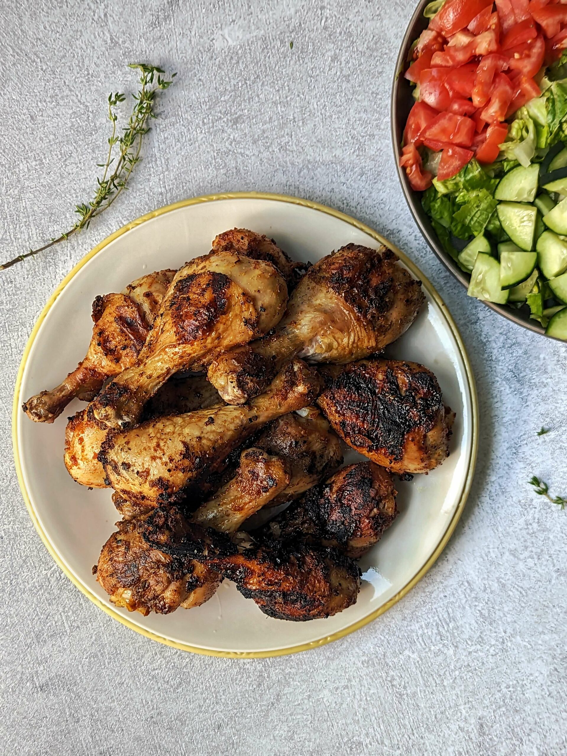 A plate full of grilled chicken drumsticks each with a perfect char and a tossed salad in the background.