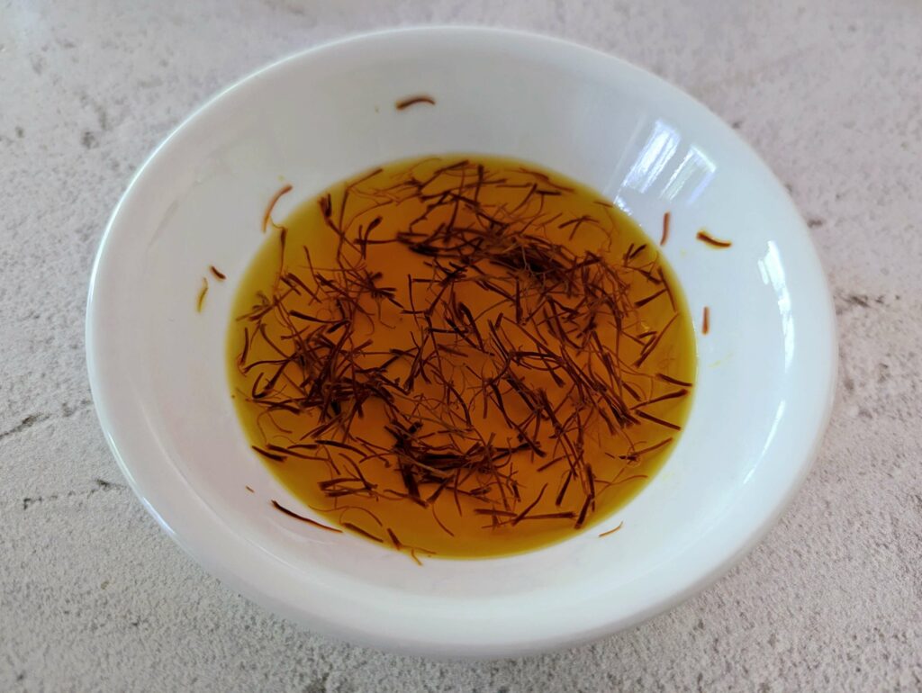 Saffron threads blooming in warm liquid in a small bowl.