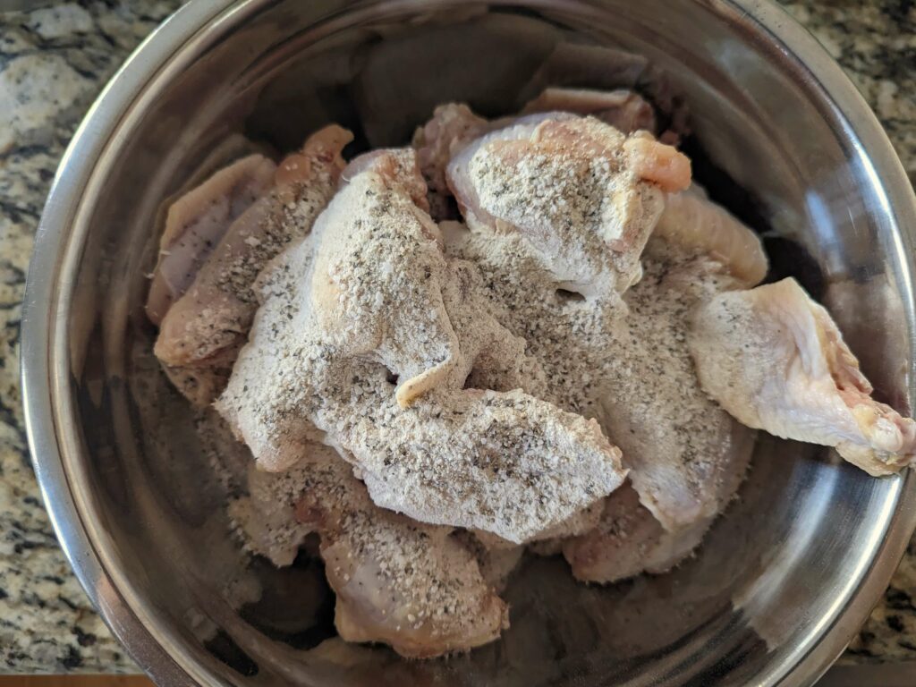 Wings tossed with the spices in a mixing bowl.