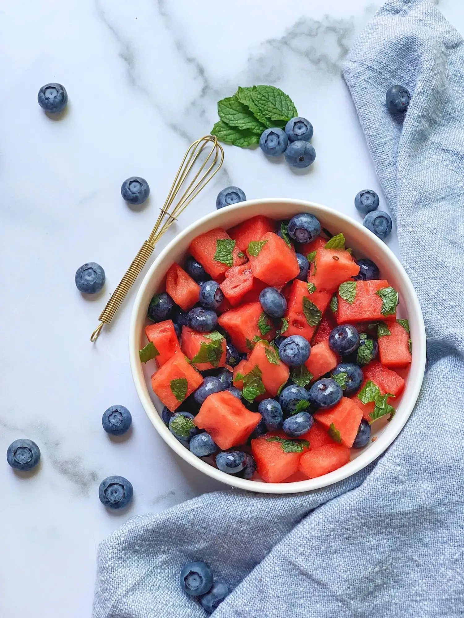 A bowl of fresh fruit surrounded fresh blueberries.