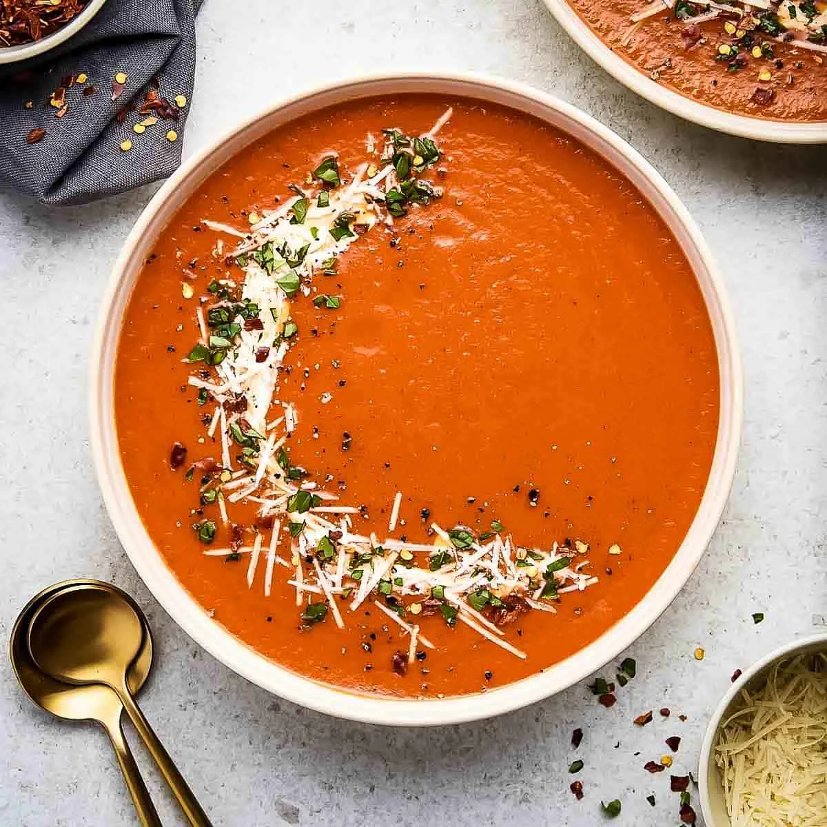 A close up of a bowl of roasted red pepper soup topped with cheese and basil.