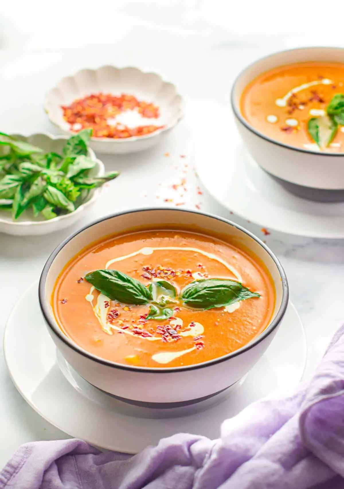 Two bowls of tomato soup topped with basil leaves.