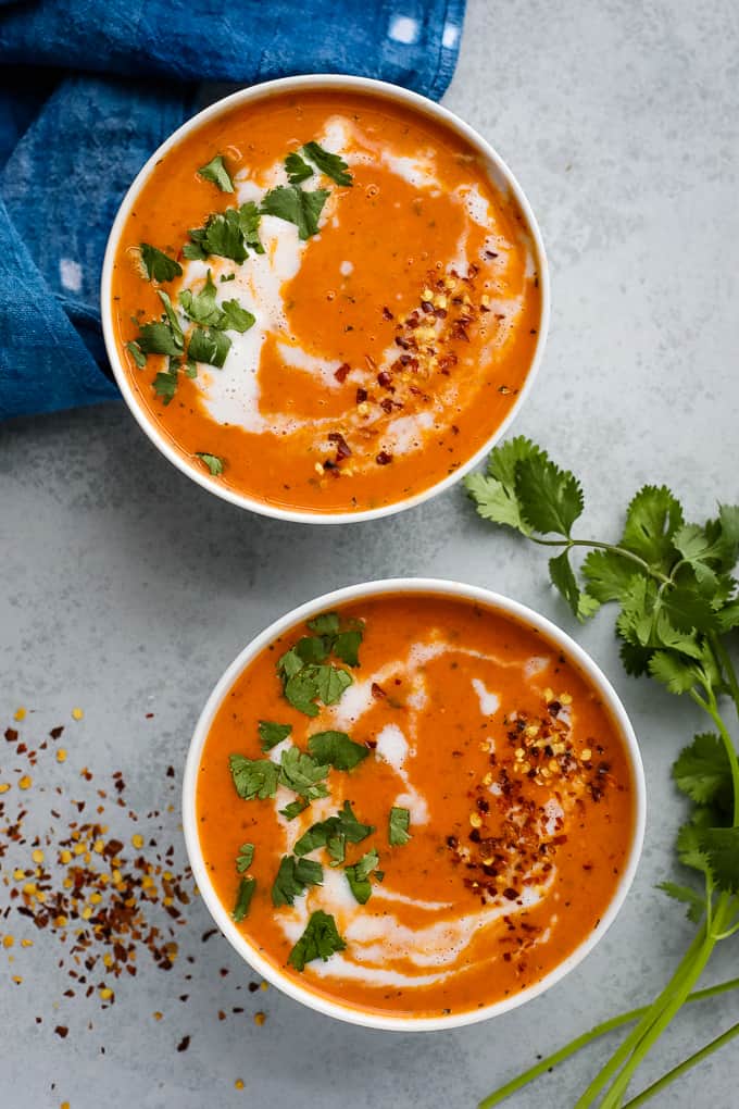 Two bowls of tomato soup topped with cream and chopped basil.