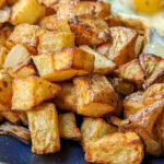 A close up of the air fryer home fries with eggs in the background.