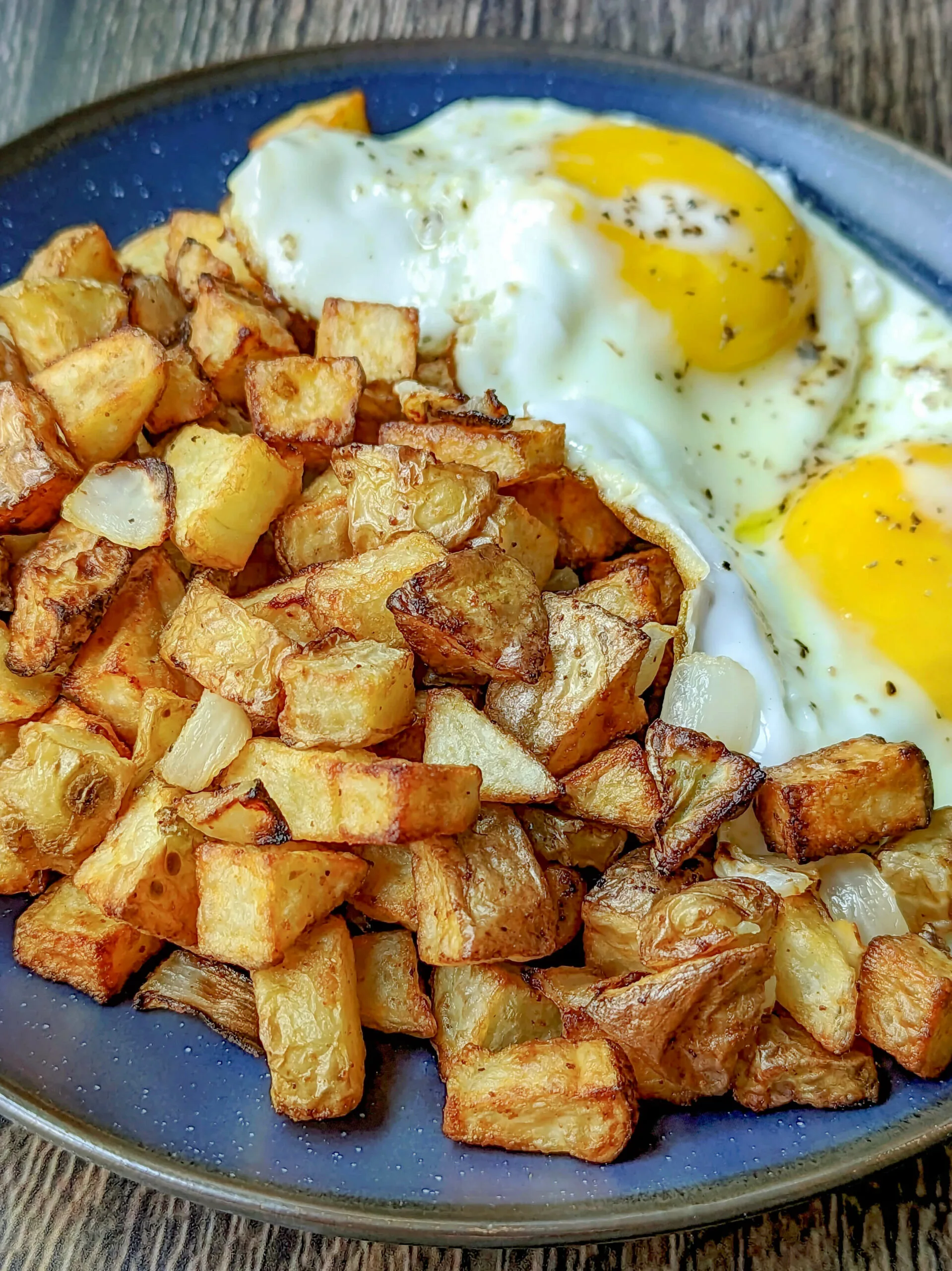 A close up of the air fryer home fries with eggs in the background.