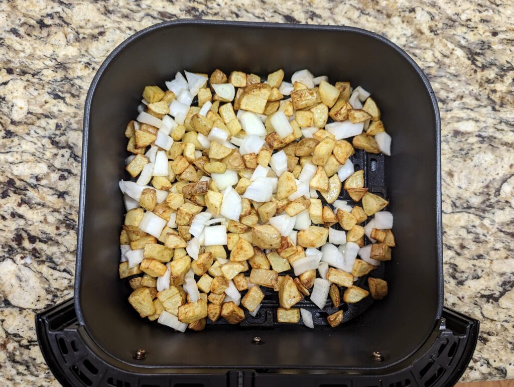 Onions added to the home fries in an air fryer basket.